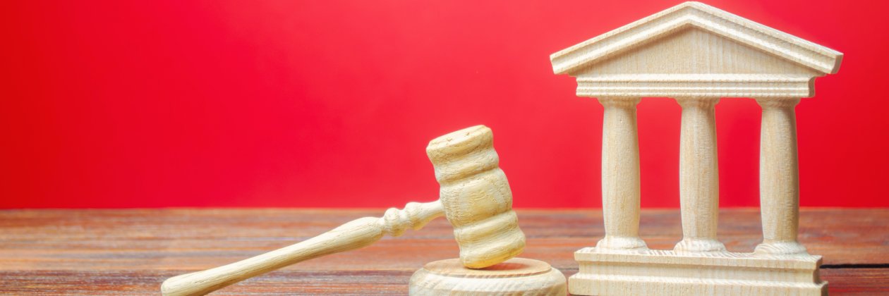 red background, wooden toy structure of a government building, wooden toy gavel. 