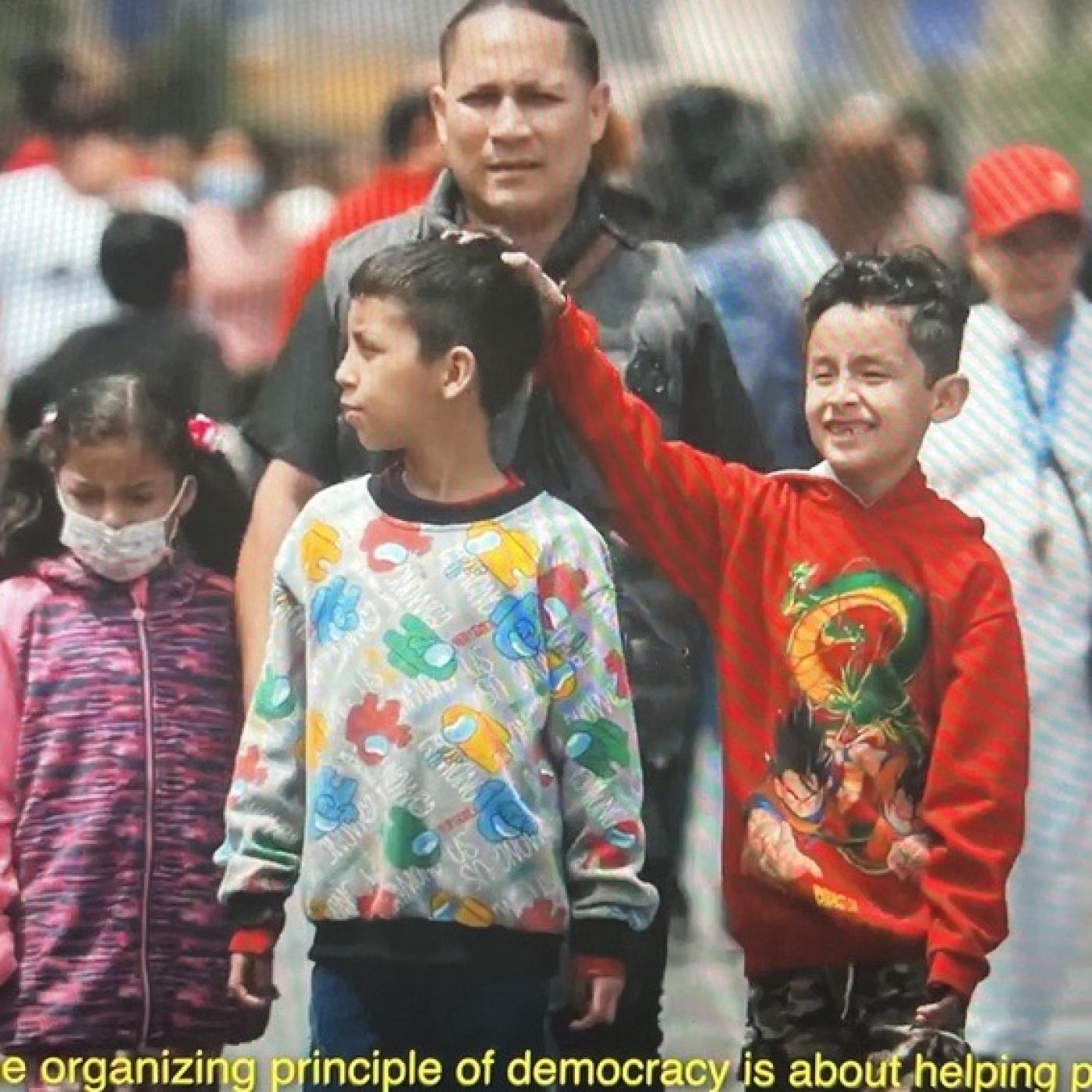 Family walking through crowded streets. Yellow text reads "The organizing principle behind democracy is helping people"